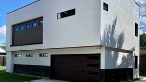 Une maison moderne à deux étages, dotée d’un toit plat, de grandes fenêtres et d’un garage.