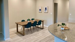 A modern dining area with a wooden table and chairs, a small kitchen island with a plant, and a framed picture on the wall. - 4-BR Getaway Ideal for Families (Richmond)
