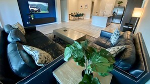 A modern living room with a black leather sofa, a coffee table, and a TV mounted on the wall. - 4-BR Getaway Ideal for Families (Richmond)