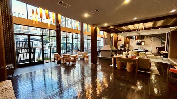 A spacious lobby with a polished wooden floor, large windows, and modern furniture.