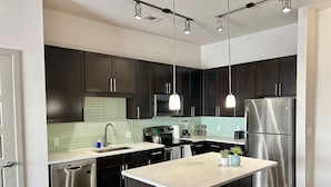 A modern kitchen with dark cabinets, stainless steel appliances, and pendant lighting.