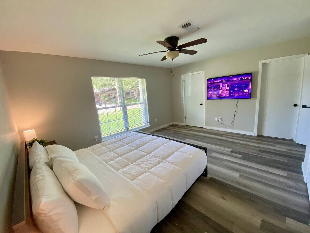 A bedroom with a bed, a ceiling fan, a TV, and a window.