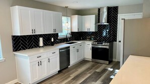 A modern kitchen with white cabinets, a black backsplash, and a stainless steel range hood. - 3 BR Getaway Ideal for Families (Houston)