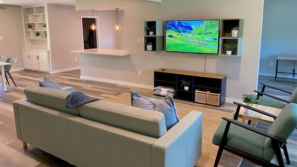 A modern living room with a sofa, chairs, a TV, and a small dining area. - 3 BR Getaway Ideal for Families (Houston)