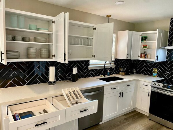 A modern kitchen with white cabinets, a black and white herringbone backsplash, a built-in dishwasher, and a stove.
