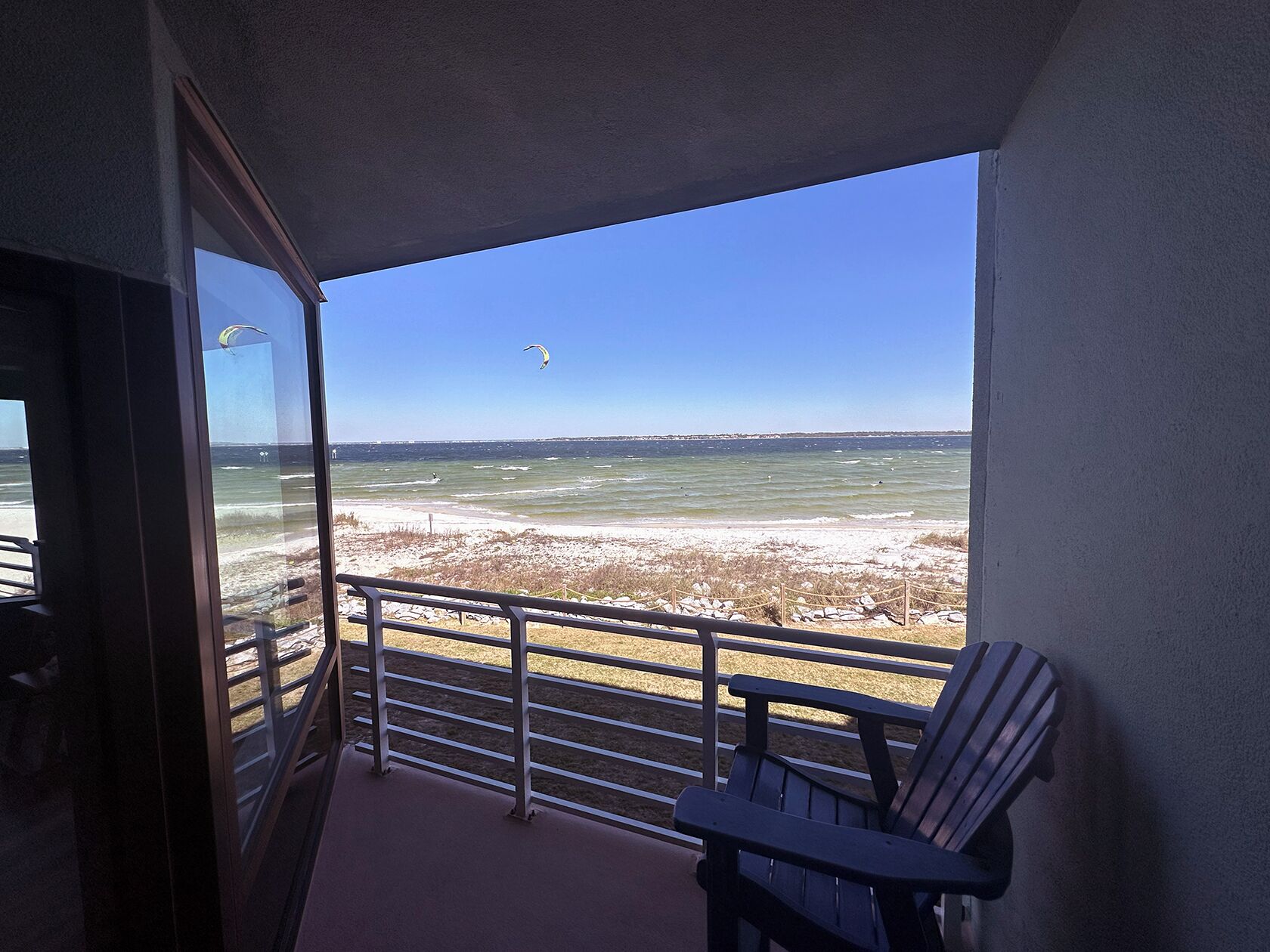 Een balkon met uitzicht op strand en zee, met een stoel en een leuning.
