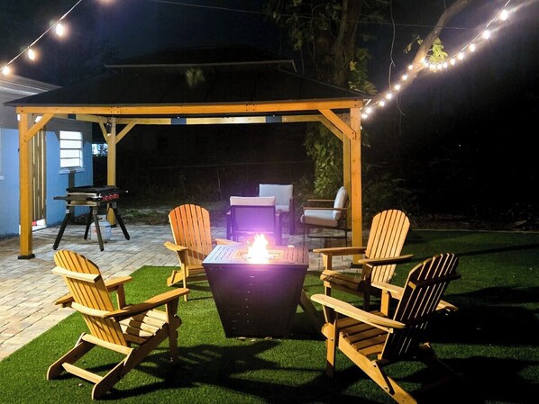 Une terrasse extérieure dotée d’une pergola en bois, d’un foyer et de fauteuils Adirondack.