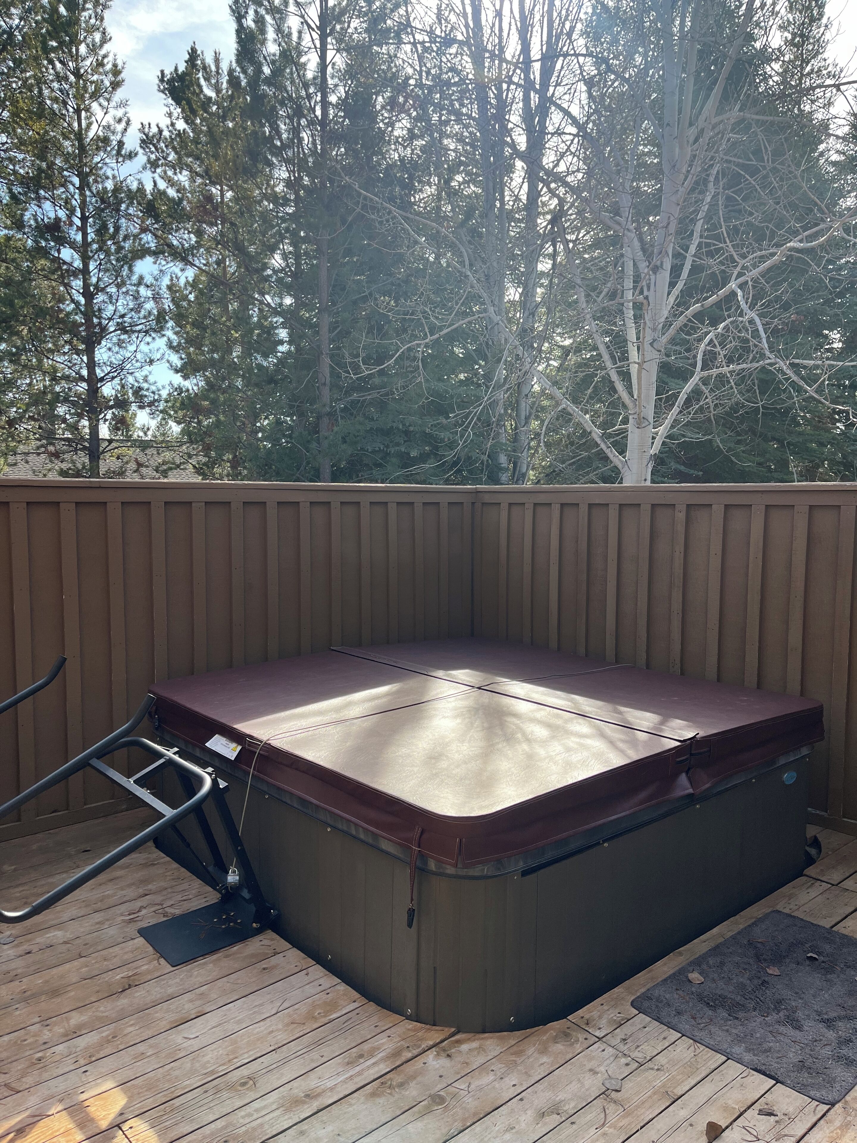 A hot tub on a wooden deck with a wooden fence and trees in the background.