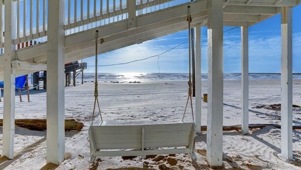 Eine Strandkabane mit Schaukel, aus weißem Holz, mit Blick auf den Ozean.