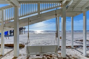 Een strandhut met een schommel, een witte houten constructie en uitzicht op de oceaan.