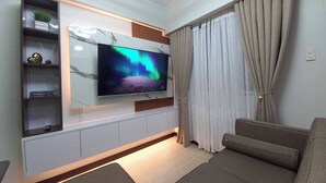 Una sala moderna con un televisor de pantalla plana montado en una pared de mármol, un sofá y una ventana con cortinas.