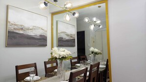 Un comedor con una mesa dispuesta para cuatro personas, rodeada de sillas, un espejo grande y obras de arte enmarcadas en las paredes.