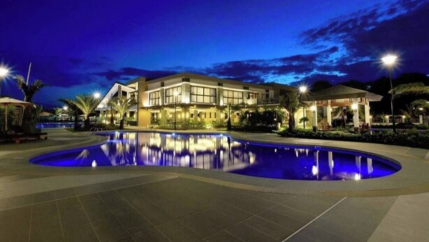 Un hotel moderno con una piscina grande y un área exterior bien iluminada durante la noche.