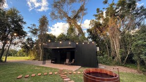 A modern outdoor structure with a seating area, surrounded by trees and a wooden barrel. - Rastro Cabins (Restinga Sêca)