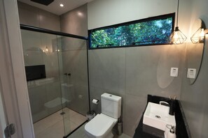 A modern bathroom with a glass shower enclosure, a toilet, a sink with a black countertop, and a wall-mounted TV.
