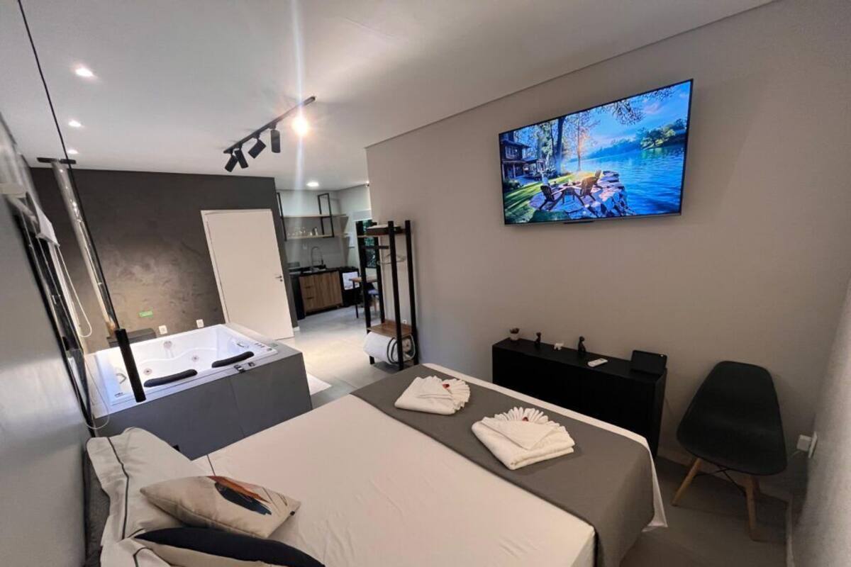 A modern hotel room with a bed, a TV displaying a scenic landscape, a small desk, and a seating area.