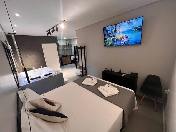 A modern hotel room with a bed, a TV displaying a scenic landscape, a small desk, and a seating area.