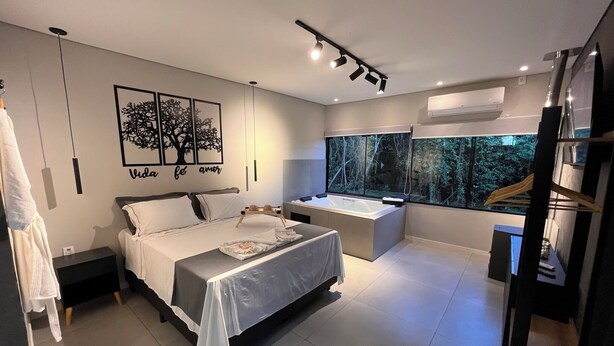 A modern bedroom with a large bed, a desk, and a view of a forest through a window. - Rastro Cabins (Restinga Sêca)