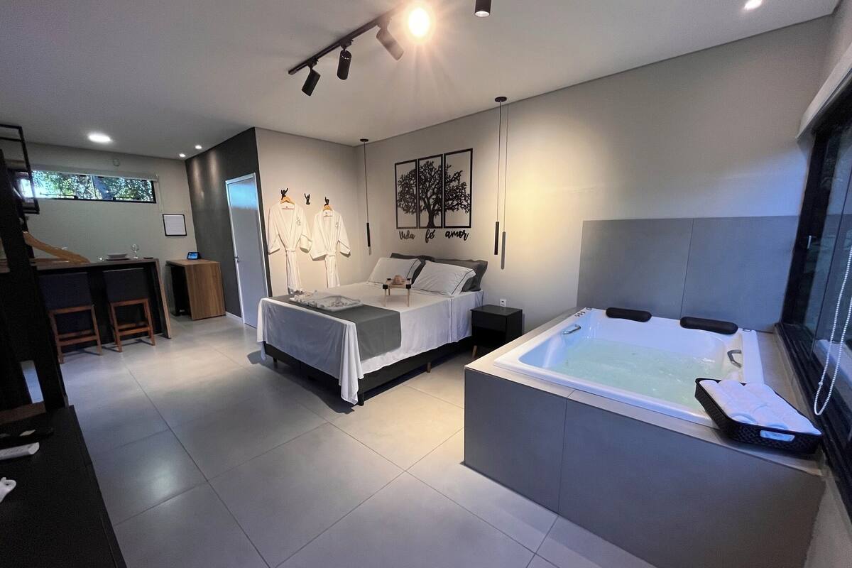 A modern bedroom with a large bed, a separate sofa bed, a bathtub, and a dining area with a bar.