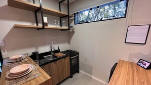 A compact kitchen with wooden countertops, a built-in stove, and a window with a view of trees. - Rastro Cabins (Restinga Sêca)