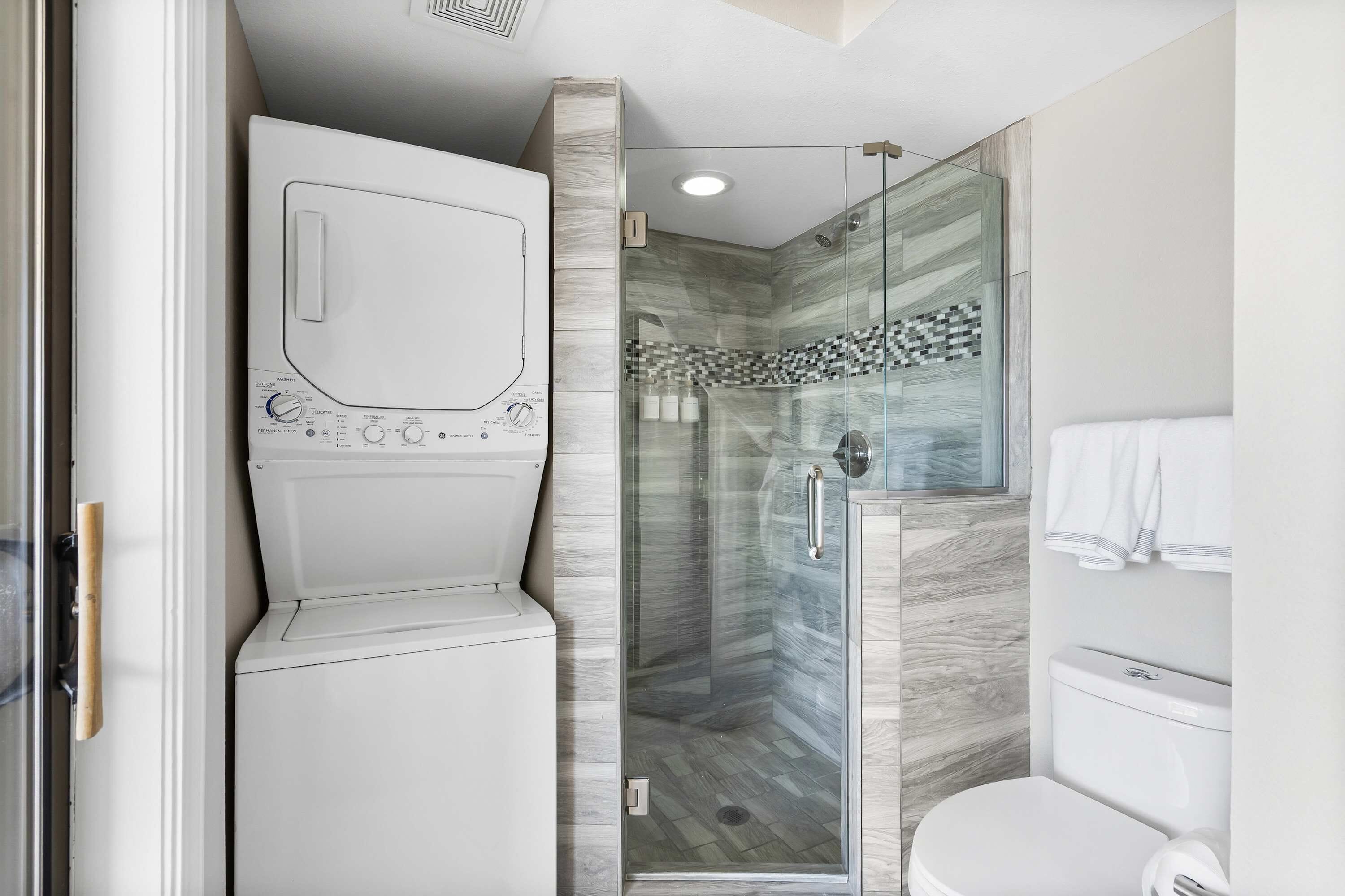 A modern bathroom with a glass-enclosed shower, a built-in washer and dryer, and a toilet.