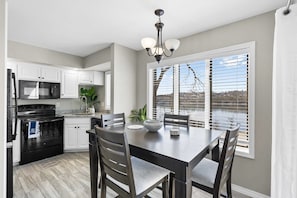 Enjoy meals in this kitchen with a dining table and four chairs, a black stove, and a chandelier above.