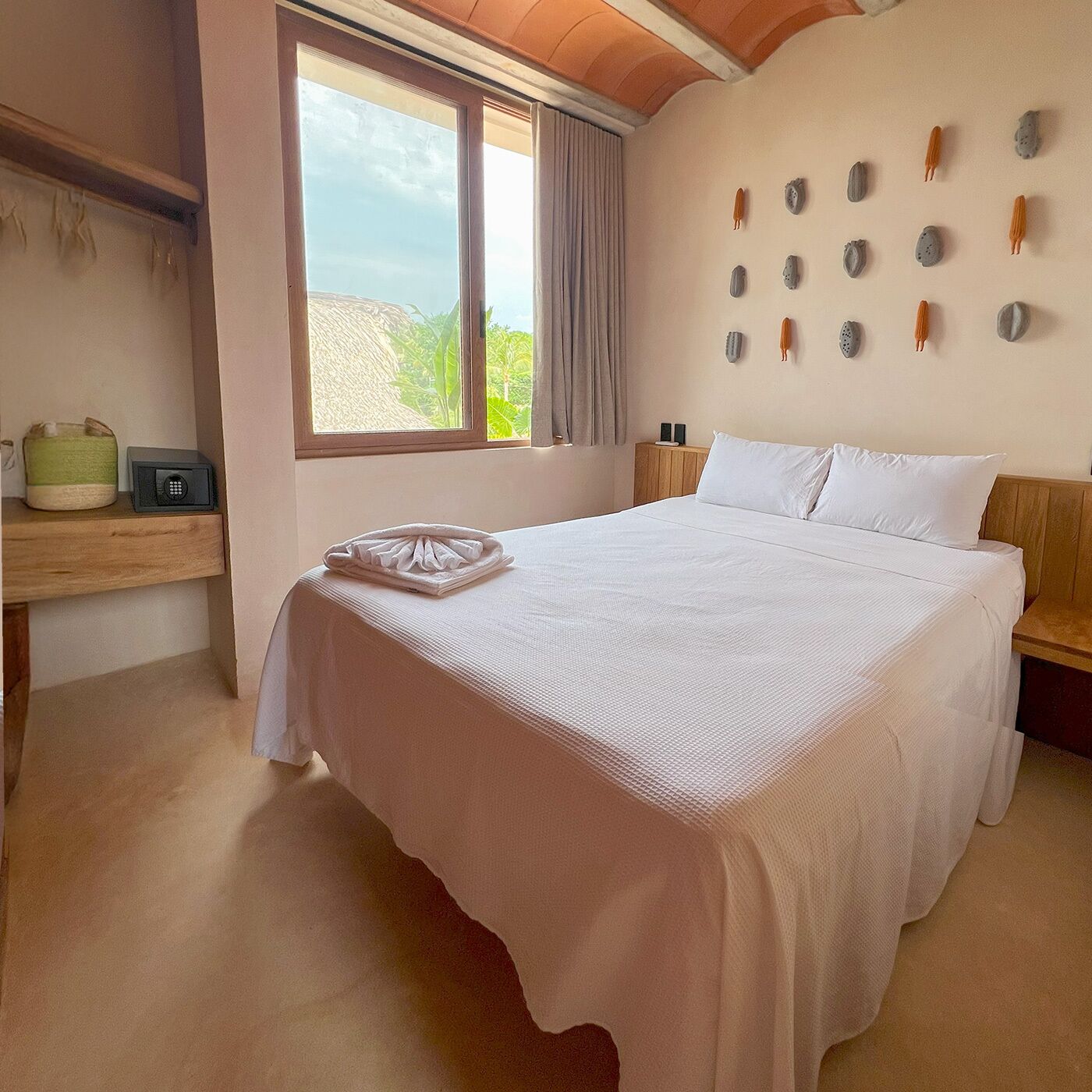 Un dormitorio con una cama grande, una ventana con cortinas, un cabecero de madera, una mesita de noche con un radio y piedras decorativas en la pared.