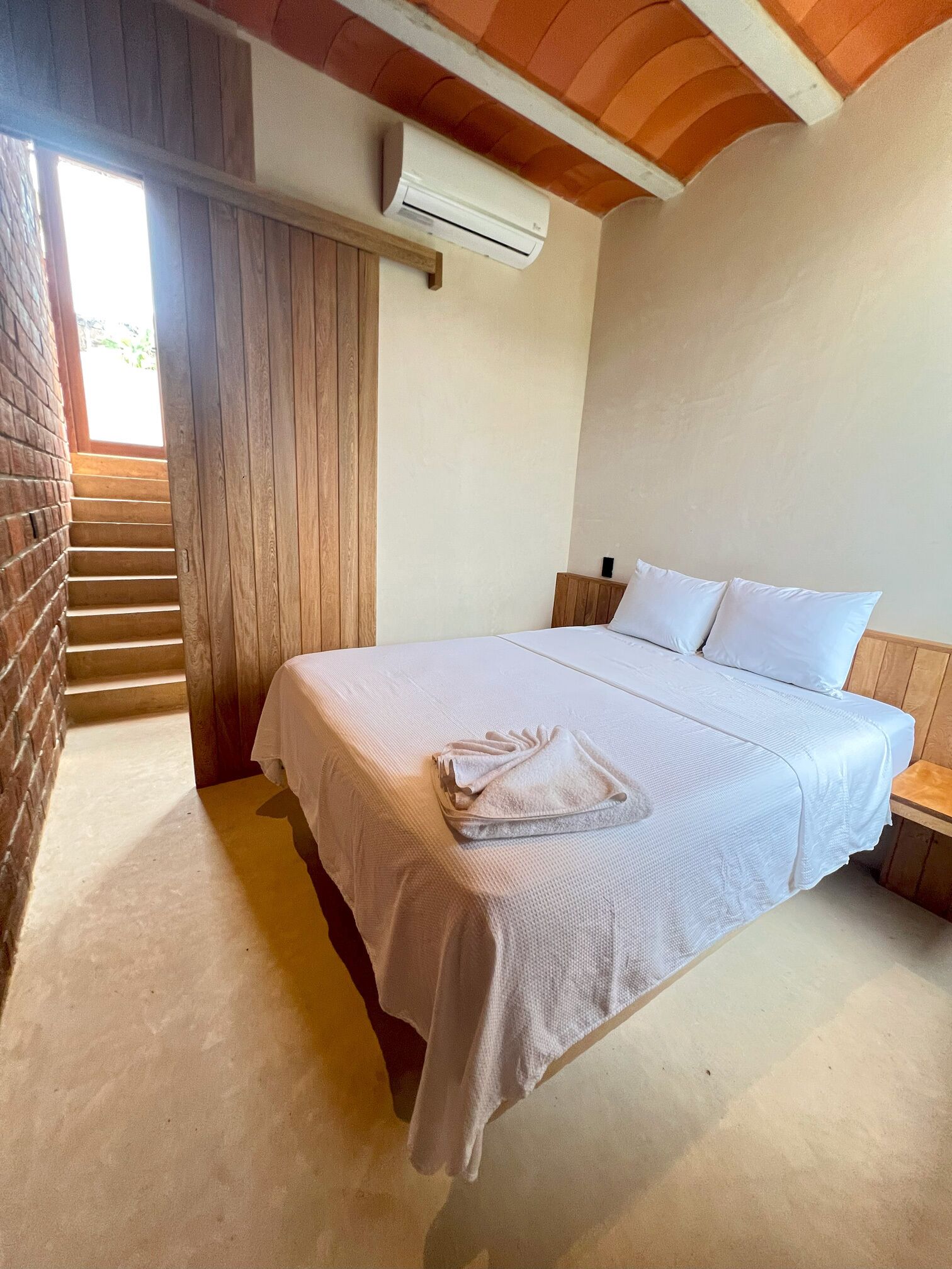 A bedroom with a bed, a nightstand, a wooden staircase, and an air conditioning unit.