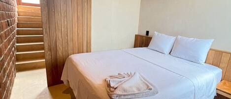A bedroom with a bed, a nightstand, a wooden staircase, and an air conditioning unit.