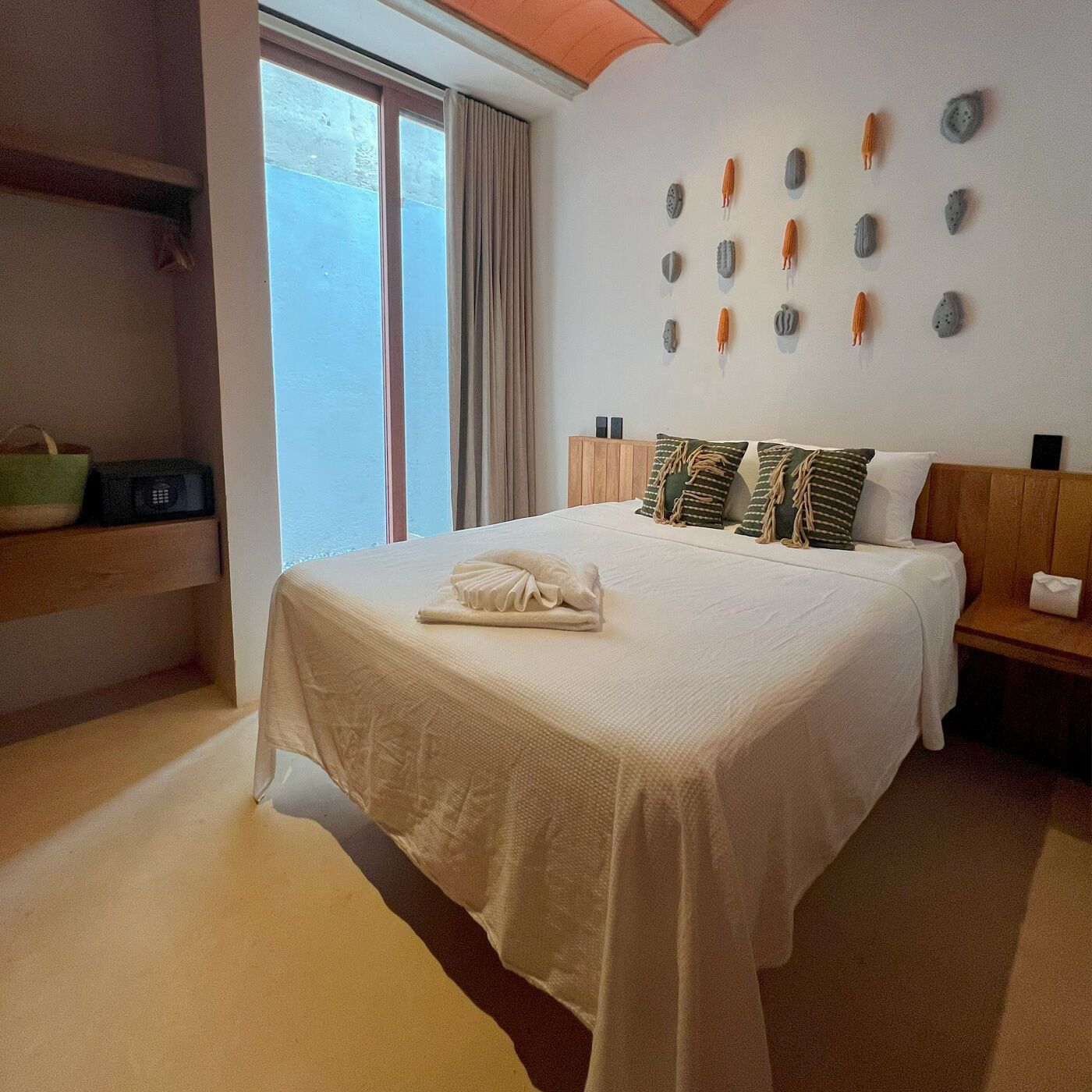 A neatly made bed with a white bedspread and two pillows, a wooden nightstand with a lamp, and a wall with decorative stone-like objects.
