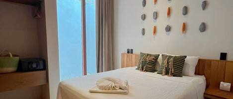 A neatly made bed with a white bedspread and two pillows, a wooden nightstand with a lamp, and a wall with decorative stone-like objects.