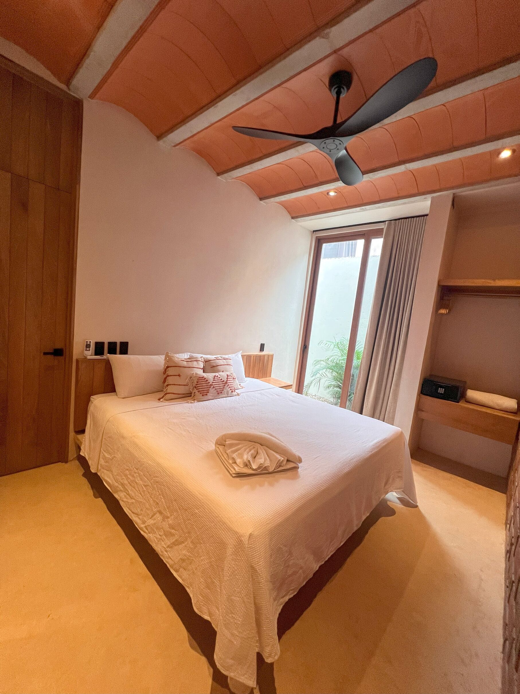 Quarto com cama, ventoinha no teto, janela com cortinas e mesa de cabeceira.