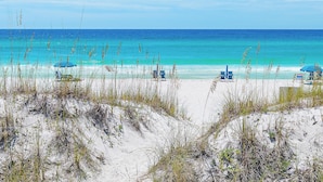 Une plage avec une eau d’un bleu limpide, des dunes de sable et des chaises de plage.