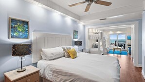 Une chambre à coucher comprenant un lit, des tables de chevet, un ventilateur de plafond et des œuvres d’art accrochées aux murs.
