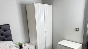Ein Schlafzimmer mit Bett, Schrank, Nachttisch mit Pflanze und kleiner Kommode.