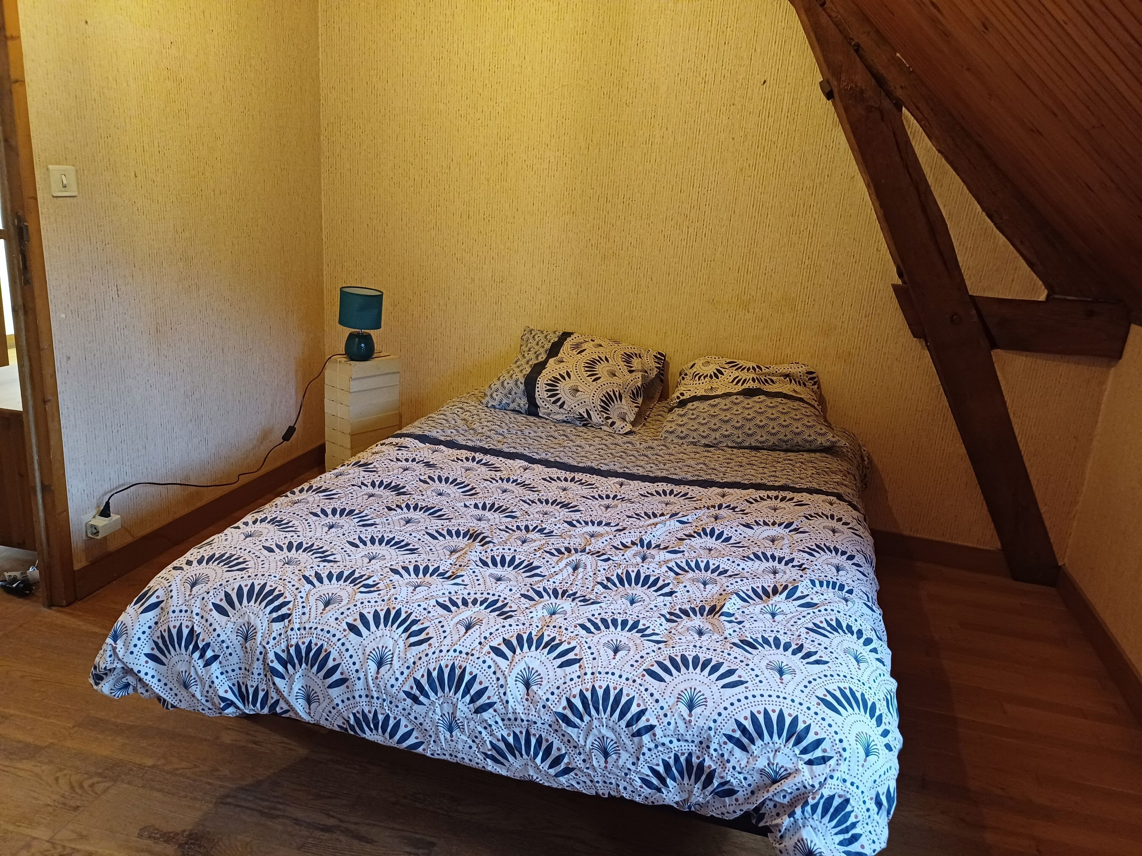 A small, cozy bedroom with a wooden ceiling and a single bed with a patterned bedspread.