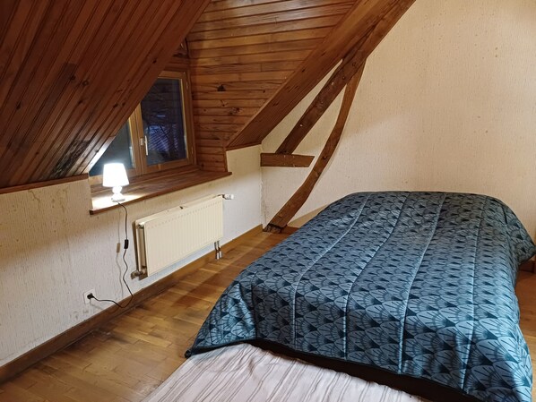 Een knus slaapkamer op zolder met schuine plafonds, een raam met lamp, een radiator en een bed met een patroongedekt.