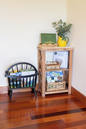Uma estante de madeira com livros e um guia de viagens, uma cesta de vime e um vaso com planta.