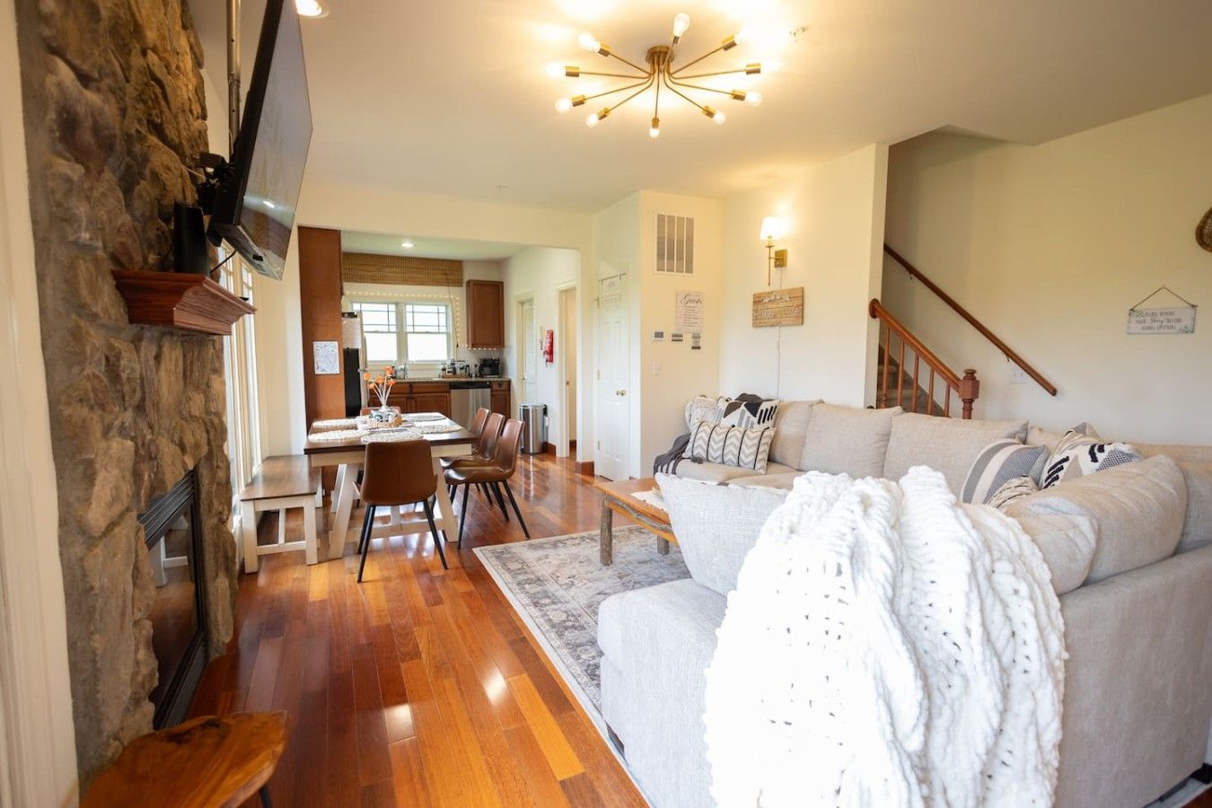 A spacious living area with a stone wall, a sofa, a dining table with chairs, and a kitchen in the background.