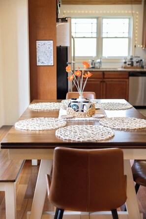 Uma mesa de jantar com jogos americanos trançados, um vaso com flores e um cardápio na parede.