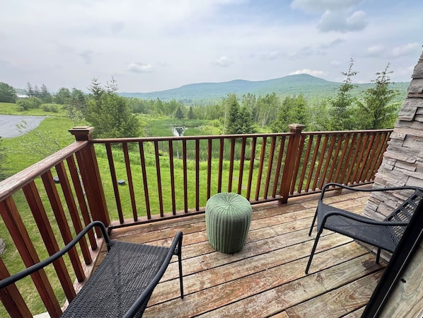 A wooden deck with a railing, two chairs, and a green ottoman.