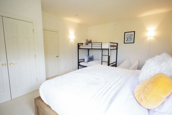 A bedroom with a bunk bed, a single bed, a white door, and a framed picture on the wall.