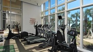 Ein Fitnessstudio mit verschiedenen Cardiogeräten, großen Fenstern und Blick auf Palmen.