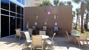 Eine Terrasse im Freien mit Korbmöbeln, Grill und einer Glaswand.