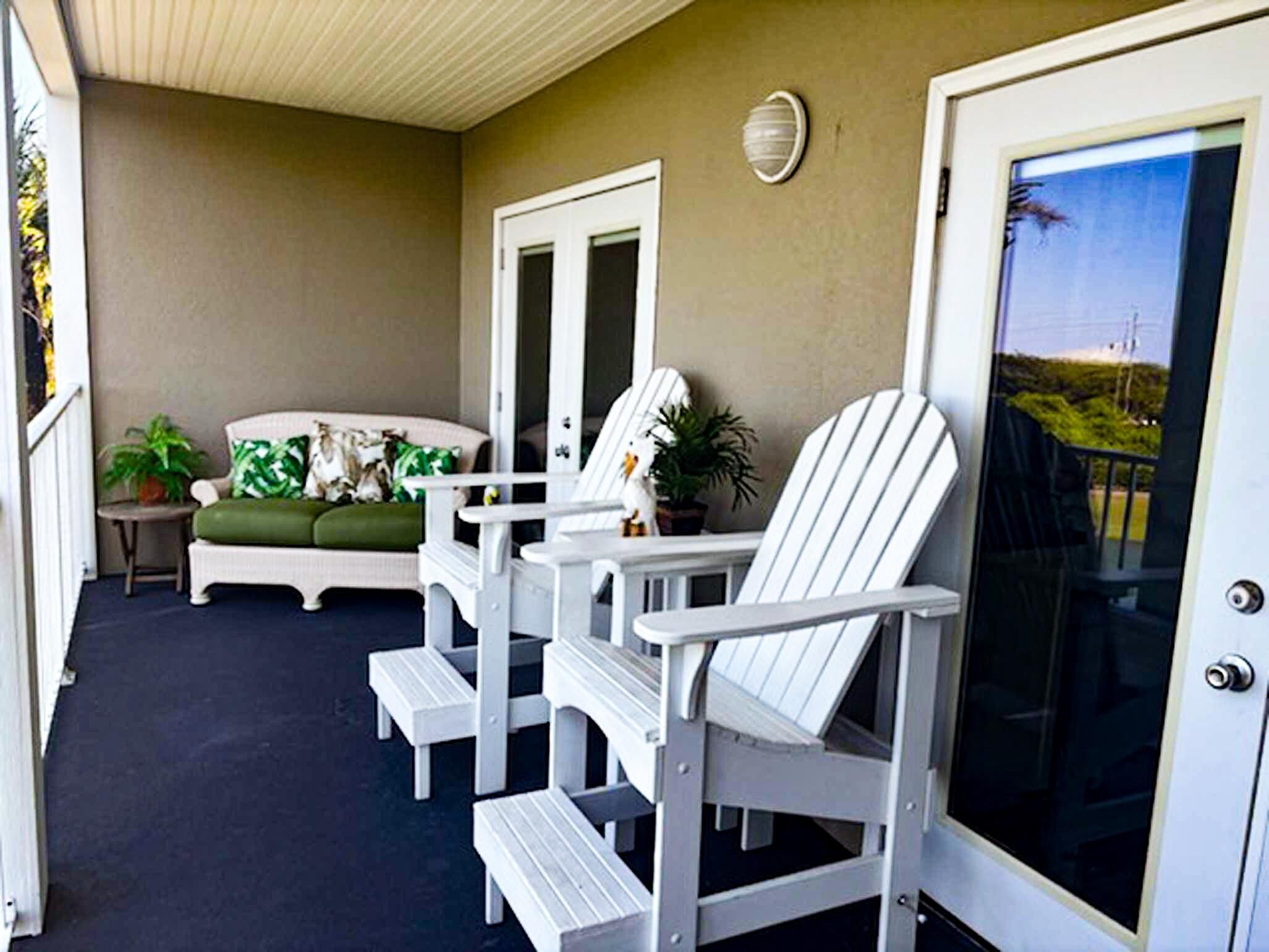 Een overdekt terras met een bank en twee Adirondack-stoelen.