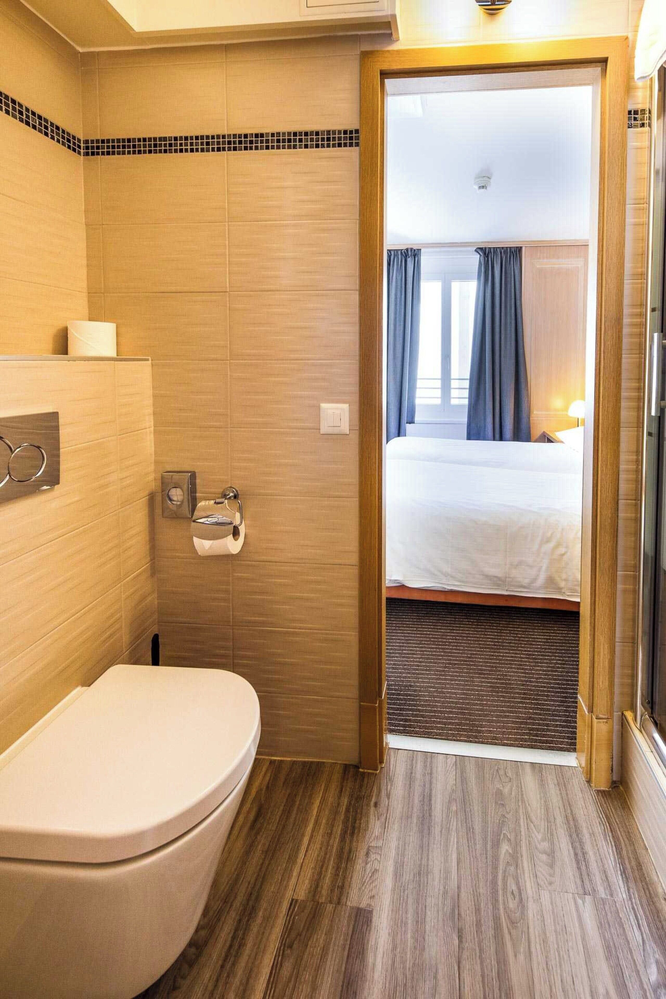 A hotel bathroom with a toilet, a towel dispenser, and a shower area.