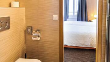 A hotel bathroom with a toilet, a towel dispenser, and a shower area.