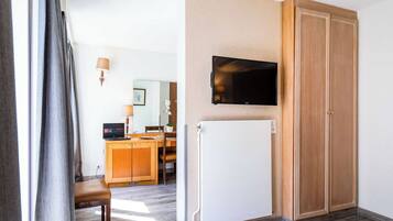 Ett hotellrum med en garderob i trä, en väggmonterad TV, ett skrivbord med en dator och ett vitt element.