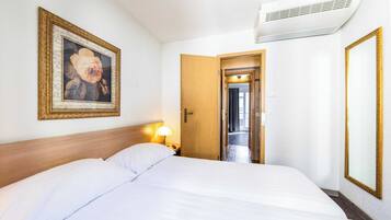 Une chambre d’hôtel avec un grand lit, un tableau encadré au mur, une porte donnant sur une autre pièce et un climatiseur fixé au mur.