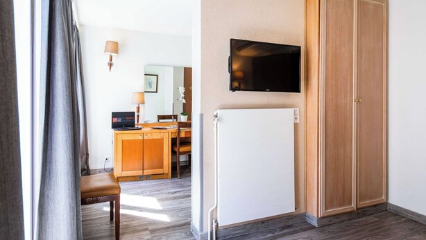 Habitación de hotel con un armario de madera, un televisor en la pared, un escritorio con una computadora y una silla.
